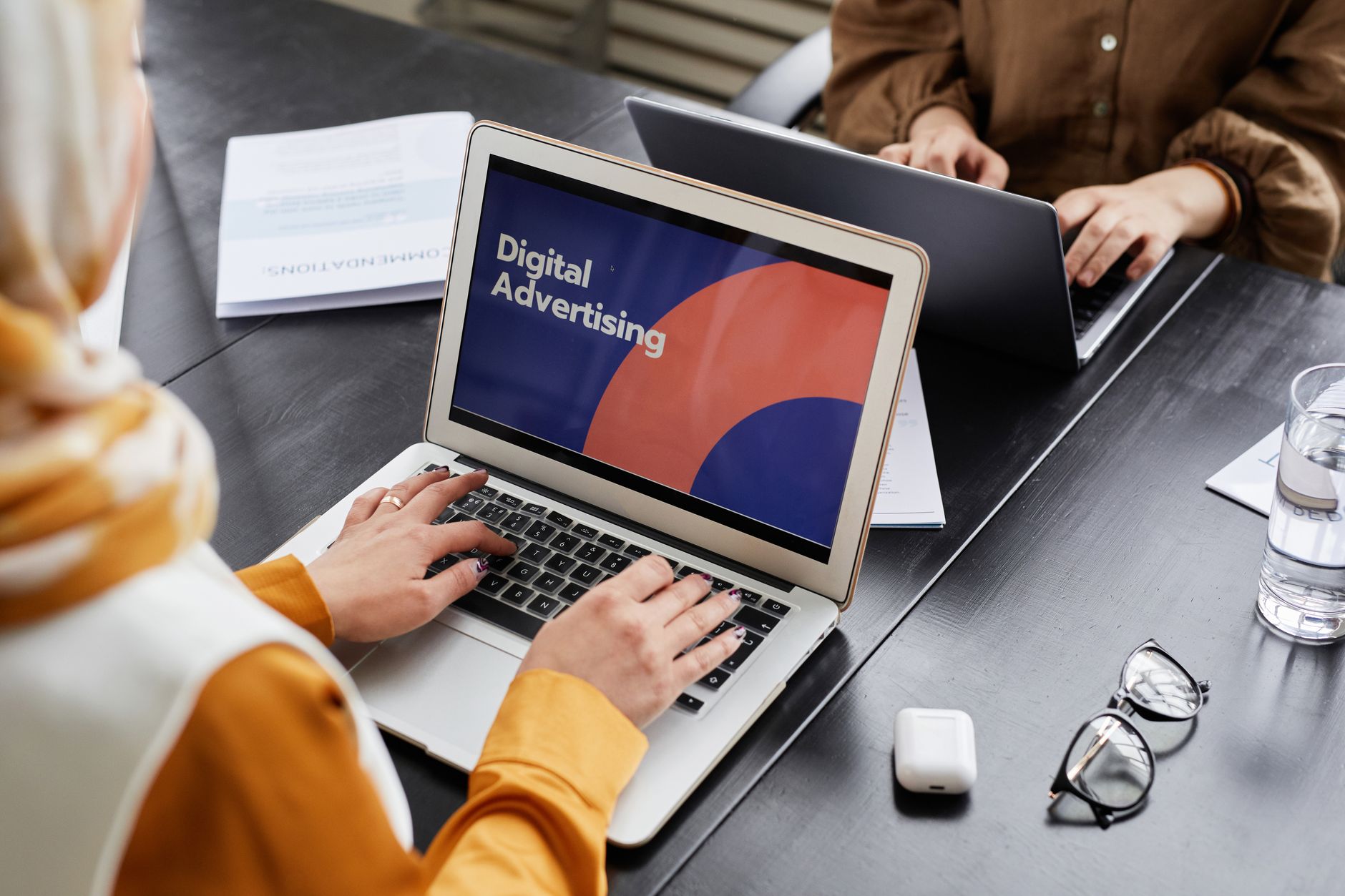 Two professionals discussing digital advertising strategy on laptops in an office setting