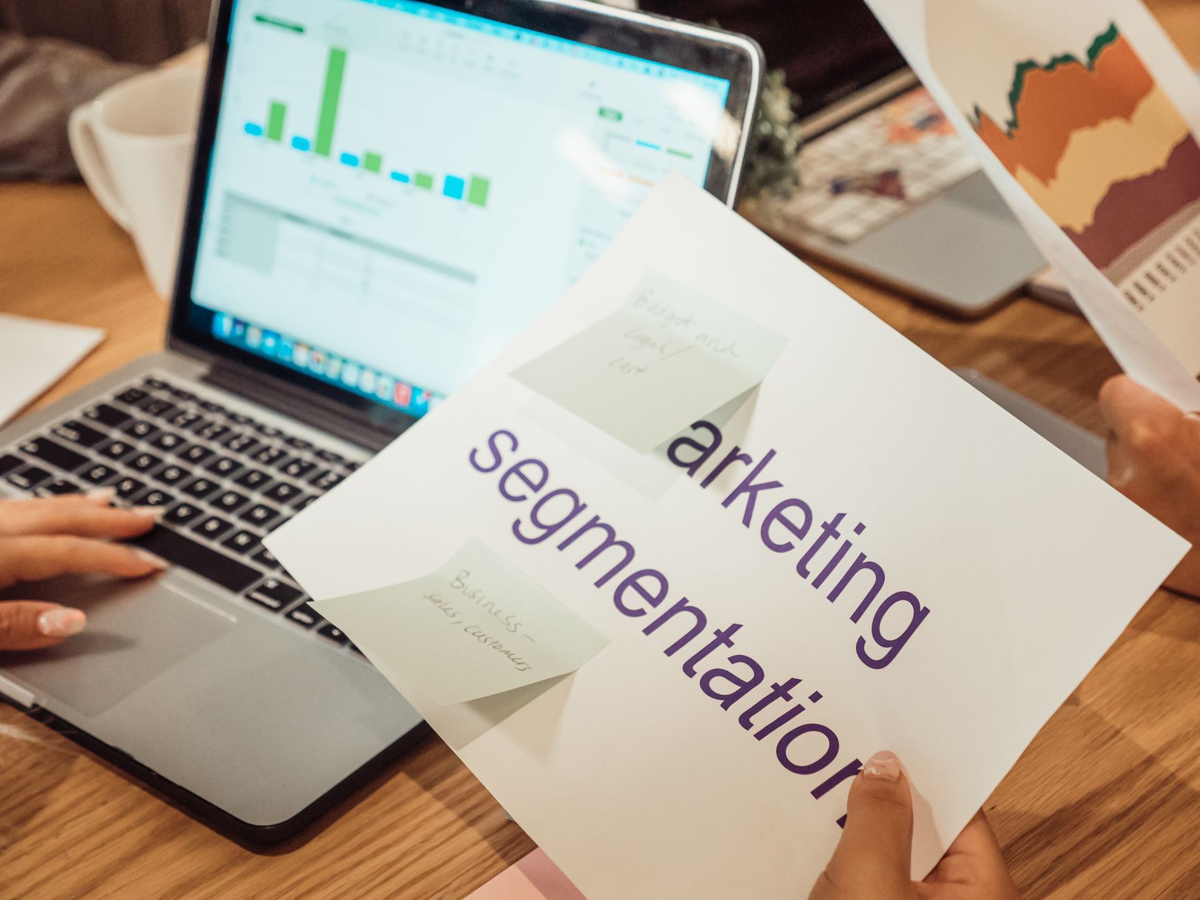 A modern workspace showing hands analyzing marketing data on a laptop and paper documents — representing Google Shopping Ads strategy analysis